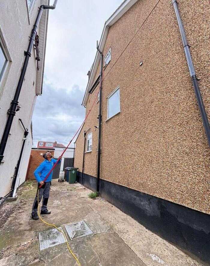 Window cleaner using a long pole in a narrow passage beside a house