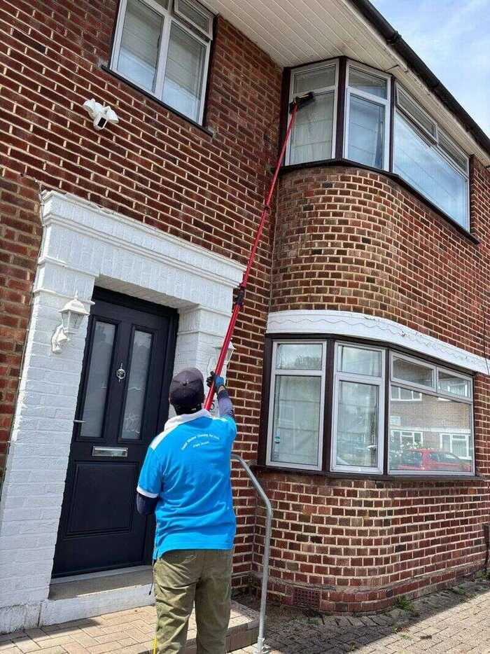Window cleaner using a water-fed pole on a red-brick bay window and front door