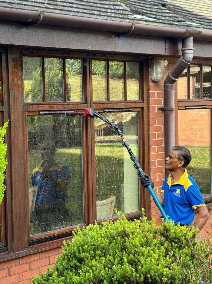 Cleaner using a water-fed pole on tall wooden-framed windows beneath a tiled roof
